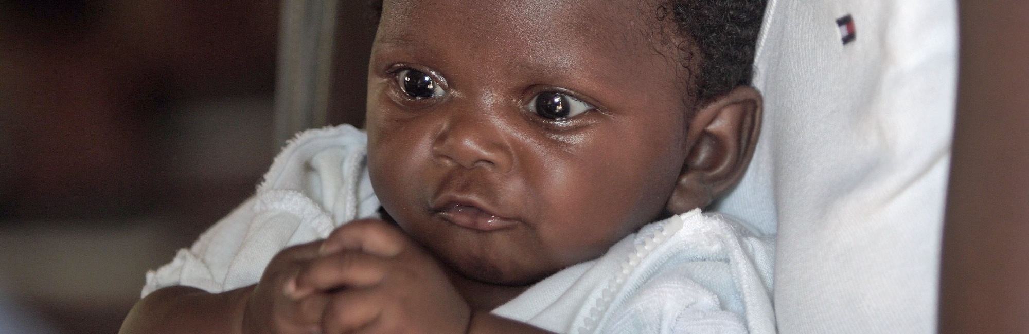 dark skinned baby in white clothes sitting on white chair