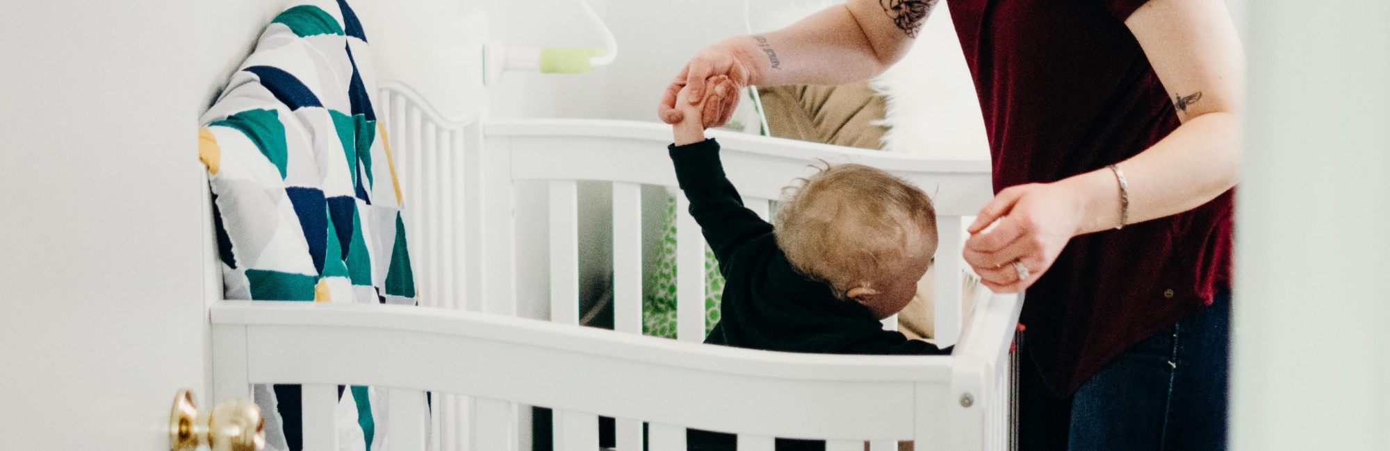 mother plays with toddler in cot during daytime