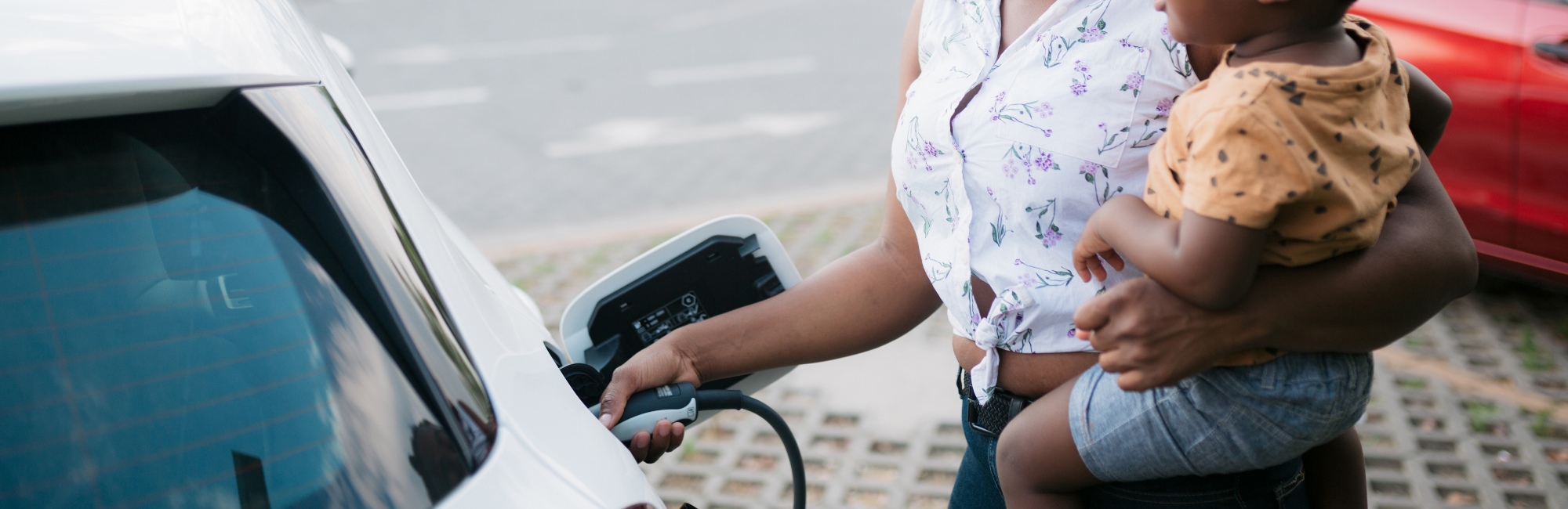mother holding toddler on her hip charges up electrical car
