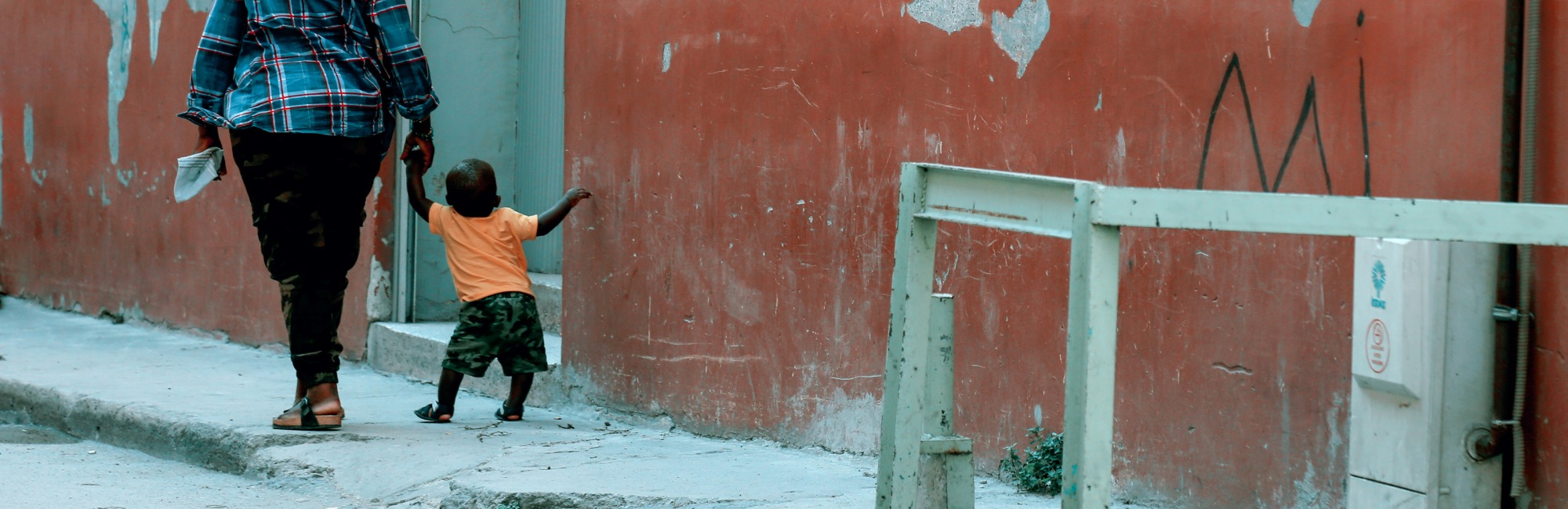 parent and toddler walk down street holding hands