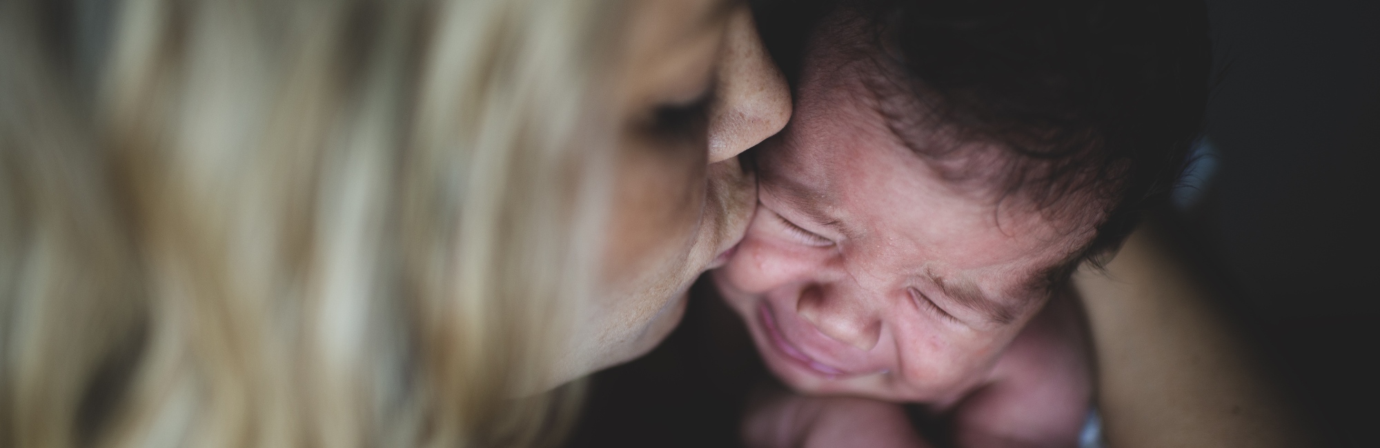 very upset baby crying as mother kisses it on cheek