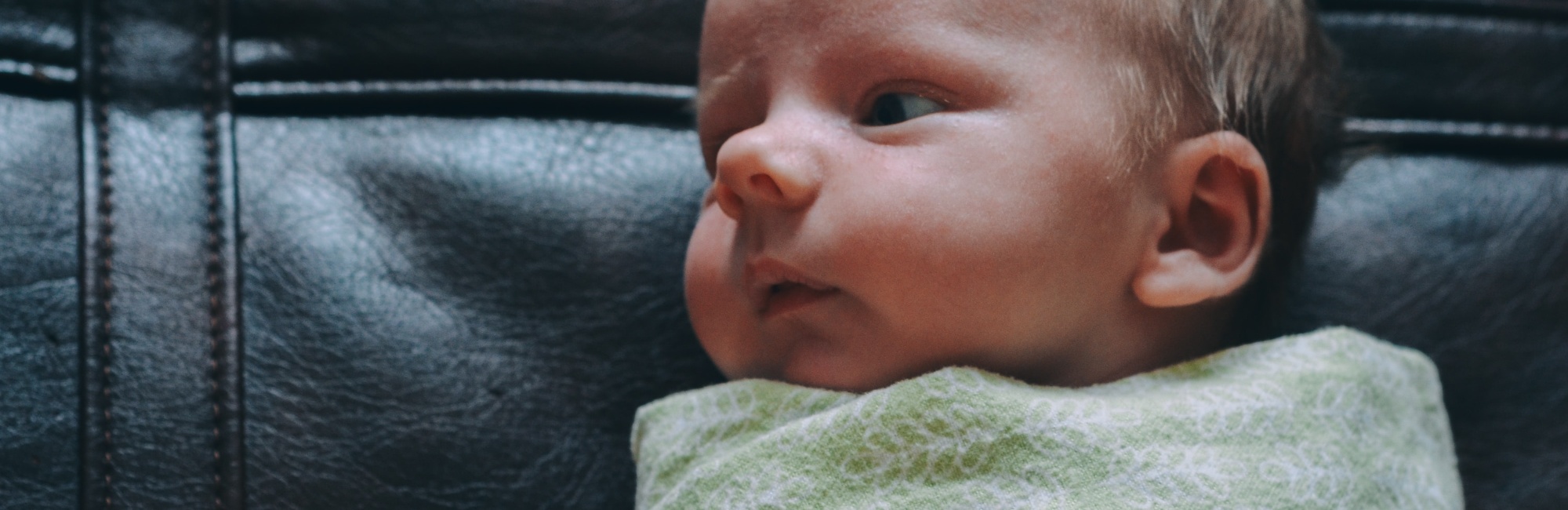 a swaddled baby awake on a couch
