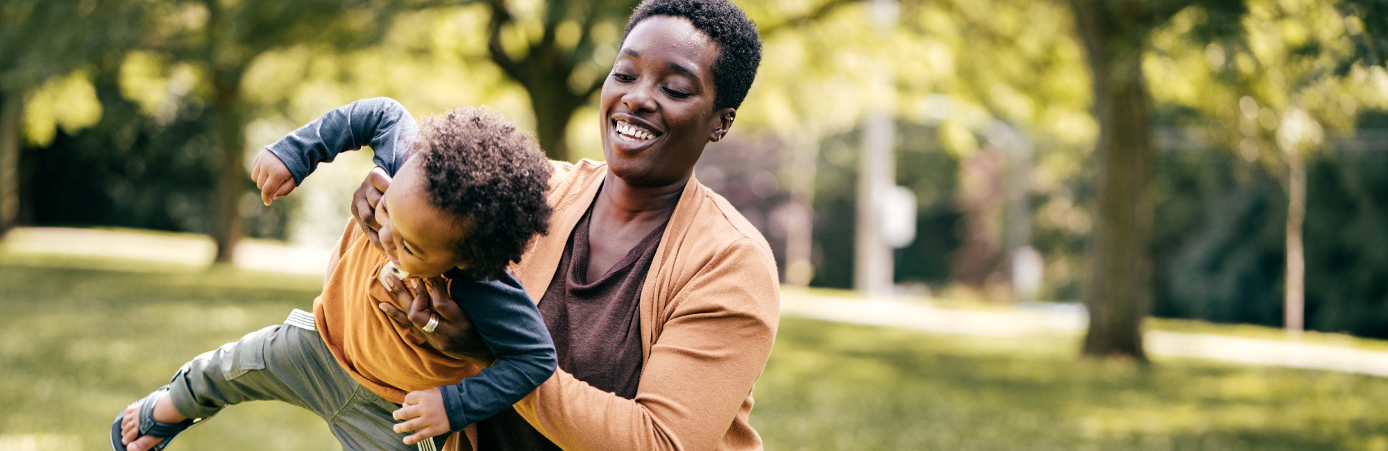 dark skinned mother plays joyously with baby outside in nature