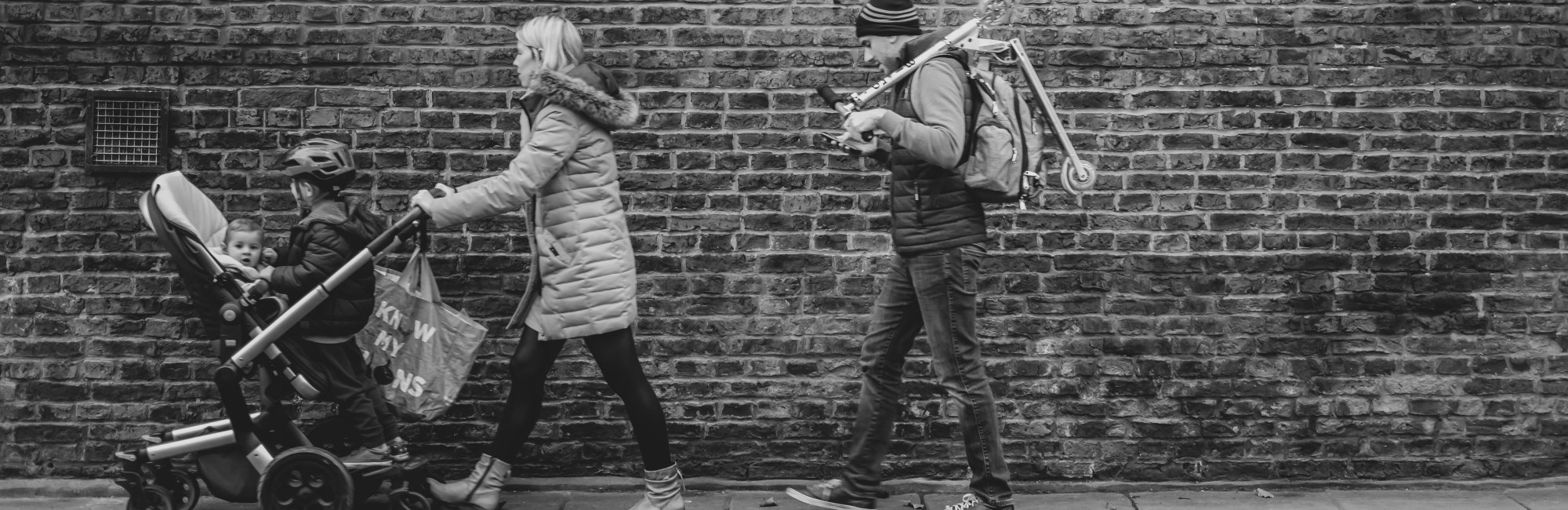 mother pushes pram with older child and baby inside it as father walks behind