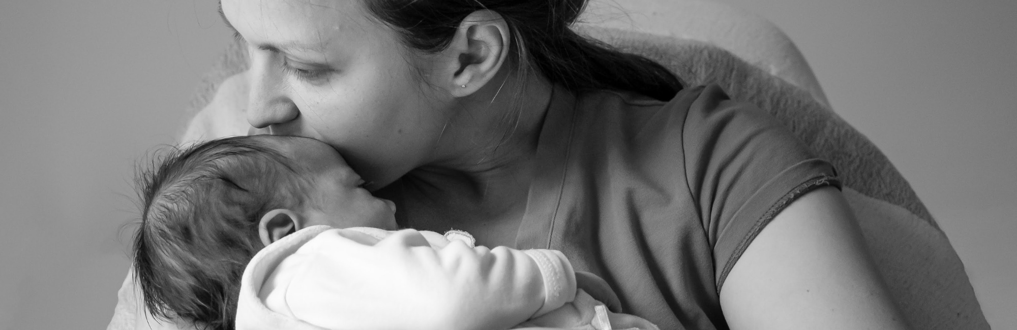 mother kisses her baby gently on the forehead as she holds it in her arms