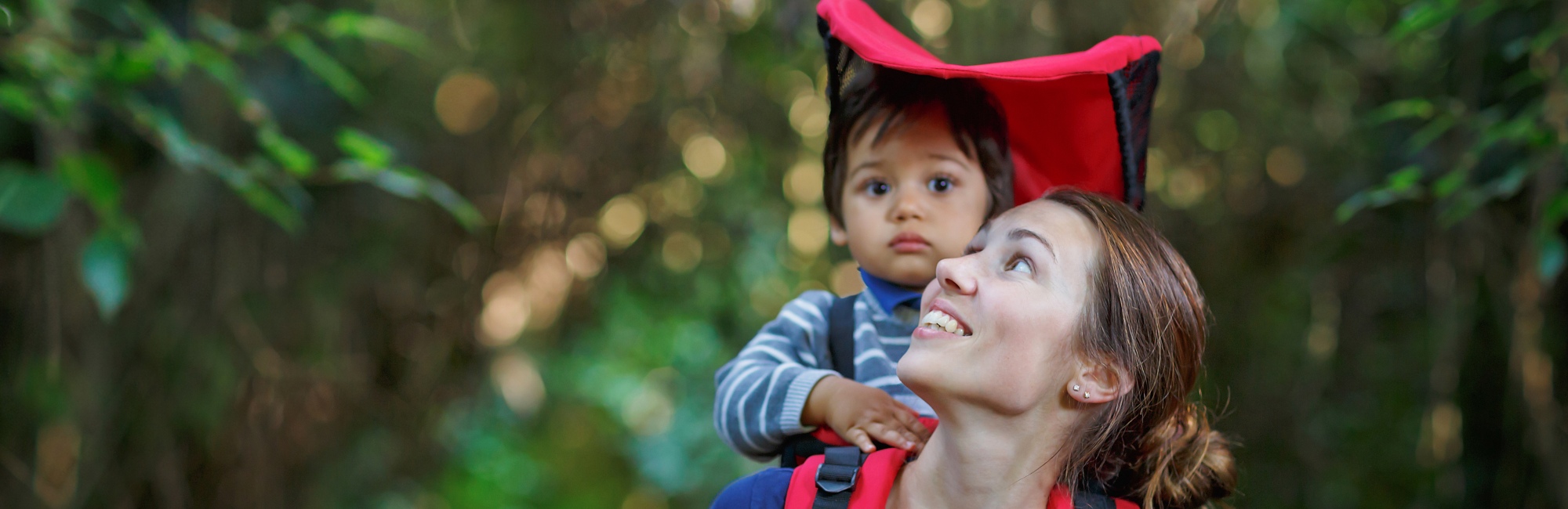 toddler carried by smiling mother walking through forest
