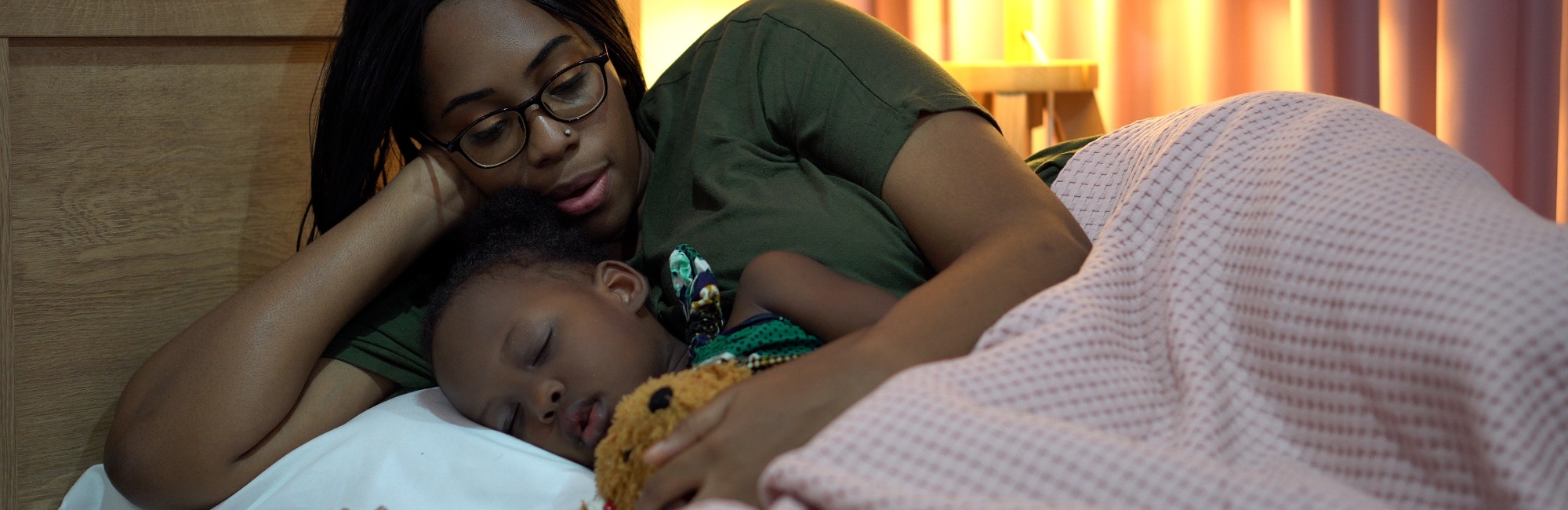 back mum with nose piercing cuddling her peacefully sleeping baby in bed