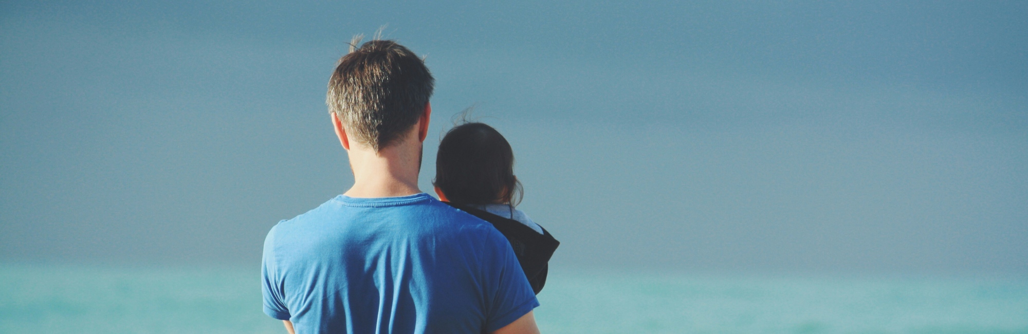 father in blue shirt holding up toddler