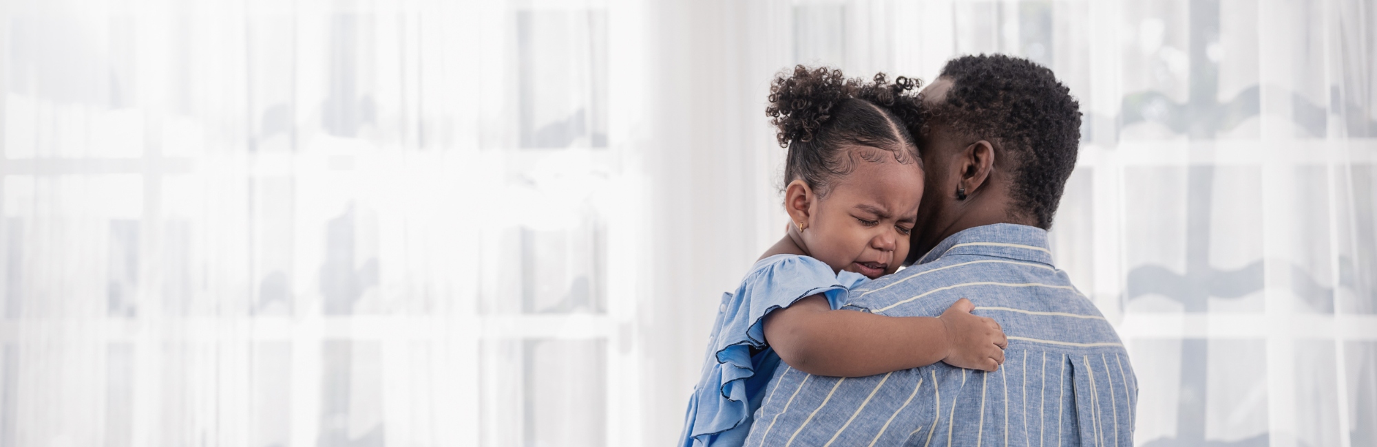 father in blue shirt holding upset young daughter