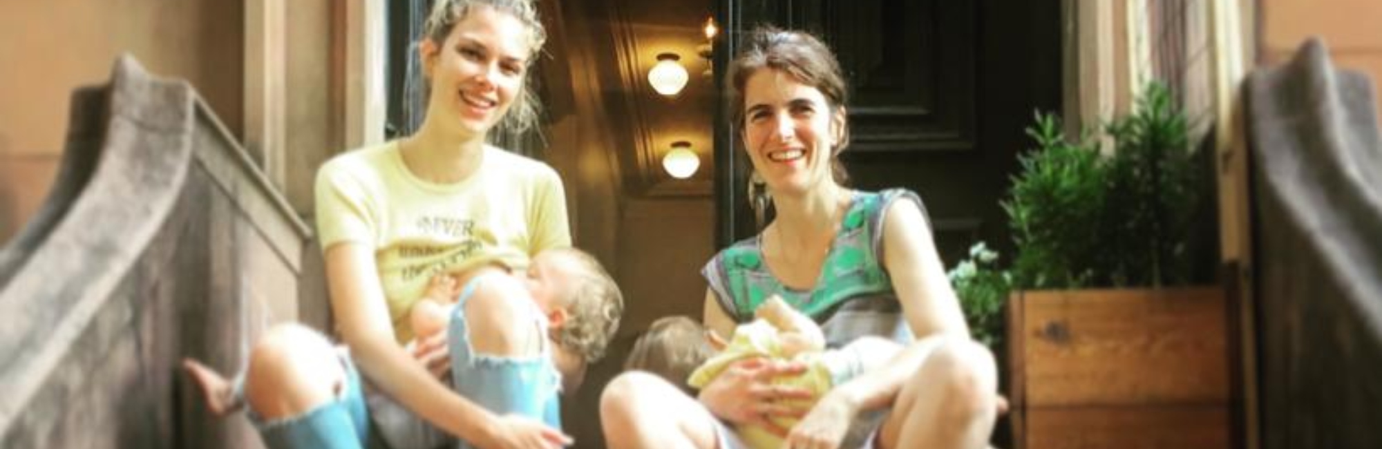two mothers breastfeed their babies outside on the front steps of a building