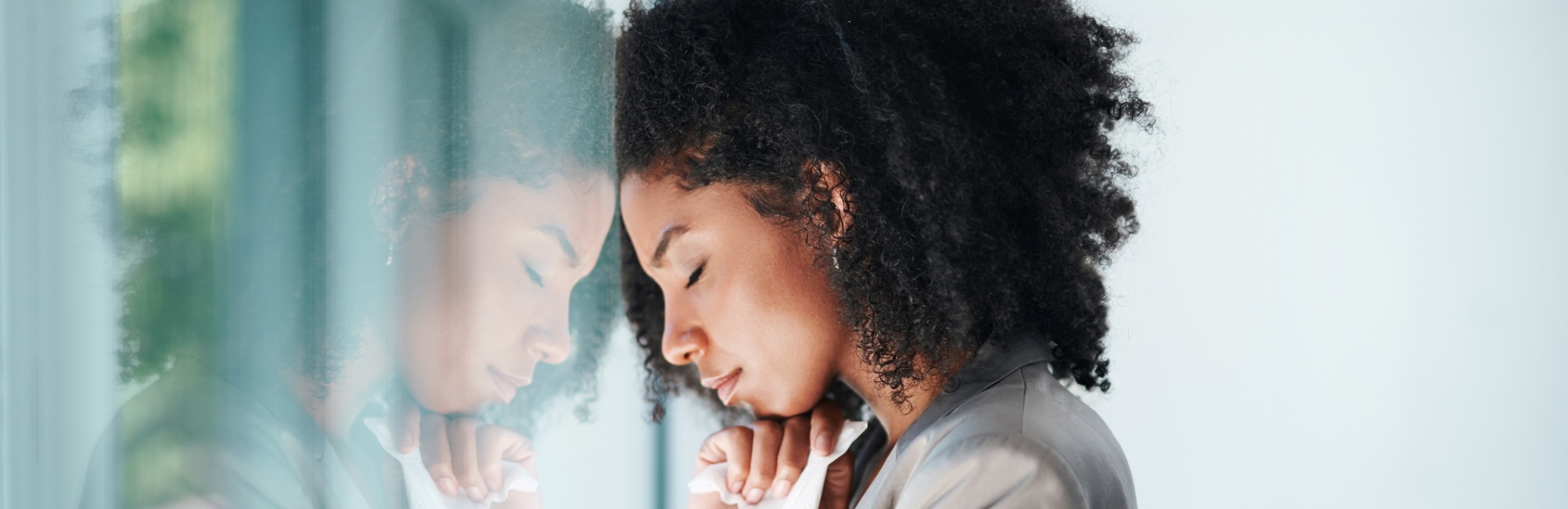 dark skinned lady with curly hair rests forehead against glass window