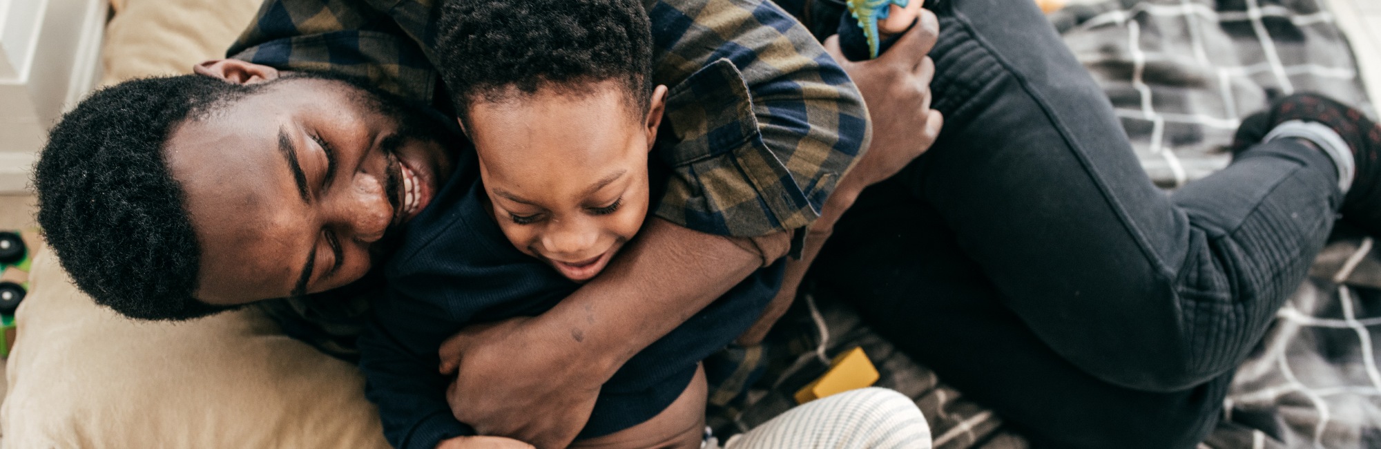 father cuddles and plays with young toddler in bed